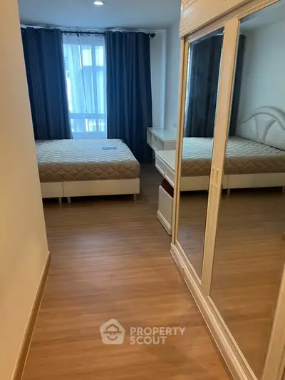 Spacious bedroom with wooden flooring and large window, featuring a comfortable bed and mirrored wardrobe.