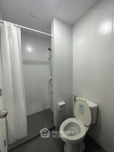 Modern minimalist bathroom with shower and toilet in sleek white tiles.