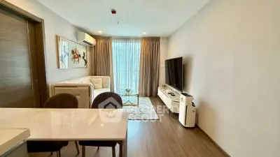 Modern living room with stylish decor, large TV, and natural light from balcony.
