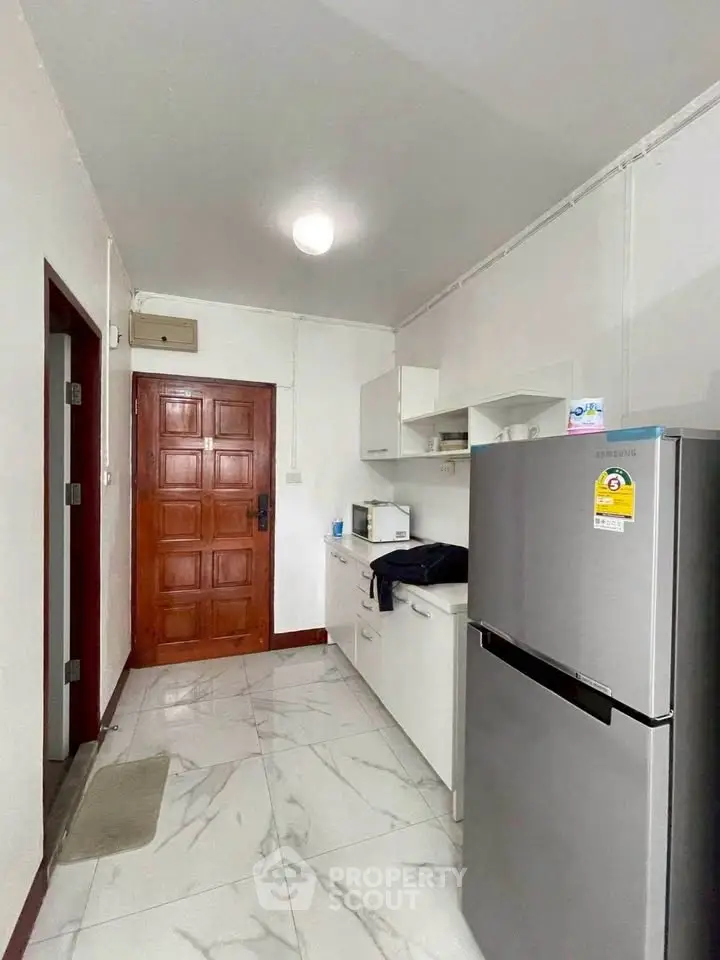 Compact kitchen with modern appliances and wooden door, ideal for small apartments.