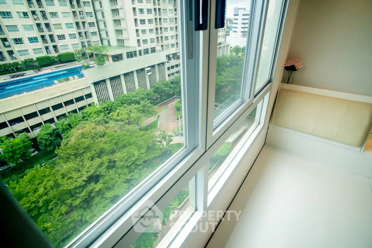 Bright apartment with large windows offering a stunning view of lush greenery and modern buildings.