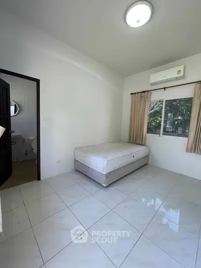 Minimalist bedroom with single bed and ensuite bathroom, featuring air conditioning and natural light.