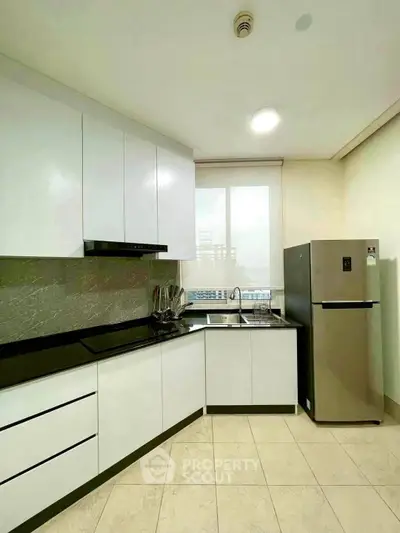 Modern kitchen with sleek white cabinets and stainless steel fridge in a bright apartment.