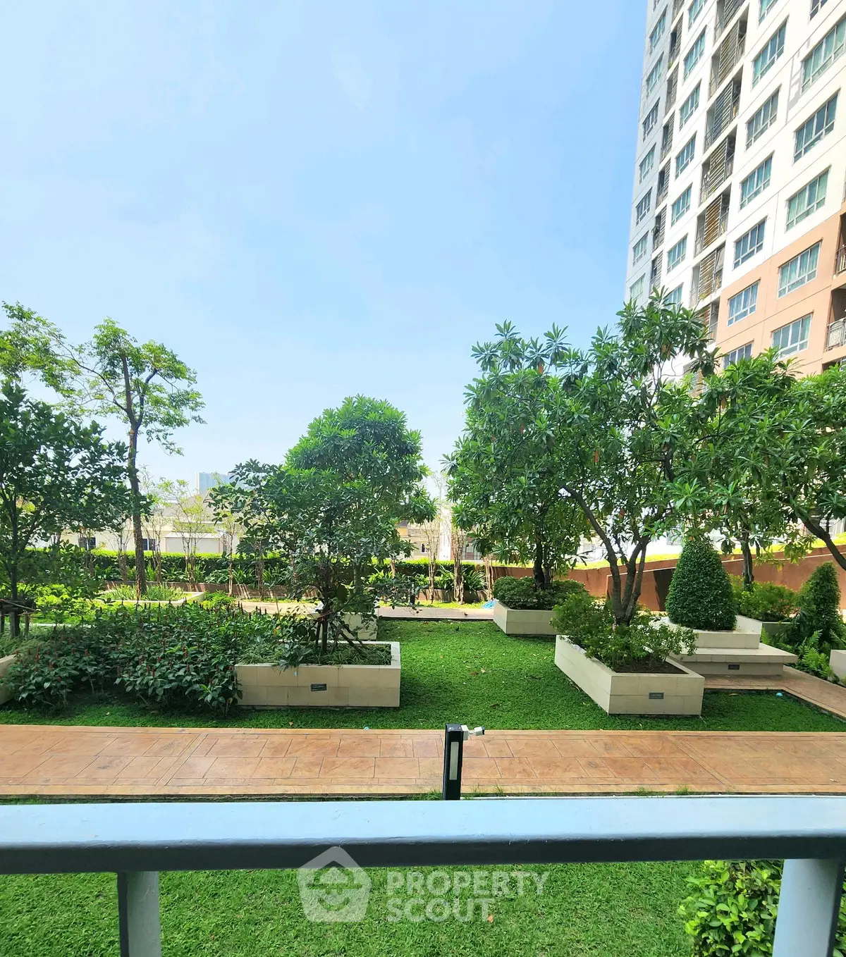 Lush garden view from a modern apartment balcony in a high-rise building.
