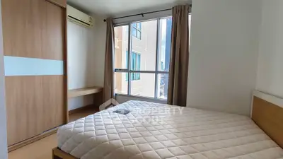 Bright bedroom with large window and modern furnishings in a high-rise apartment.