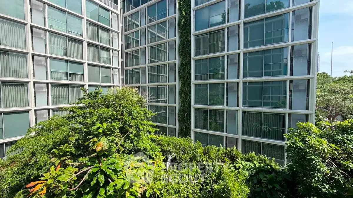 Modern apartment building with lush greenery and large windows, offering a serene urban living experience.