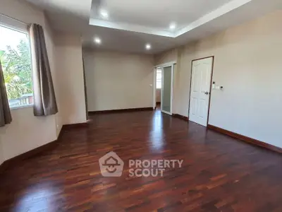 Spacious empty room with wooden flooring and large windows, perfect for customization.