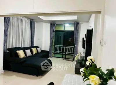 Spacious modern living room with elegant black sofa and large windows leading to a balcony.