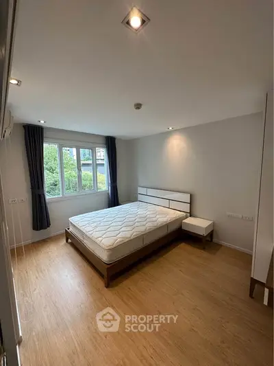 Spacious bedroom with large window and modern furnishings in a bright, airy apartment.