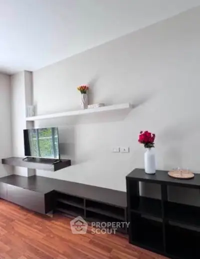 Modern living room with sleek furniture and wooden flooring, featuring a mounted TV and decorative shelves.