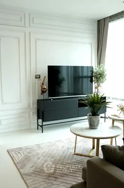 Elegant living room with modern decor and large TV, featuring stylish furniture and natural light.
