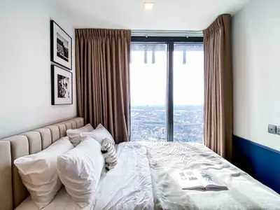 Luxurious bedroom with stunning city view from large window, elegant decor and cozy bedding.