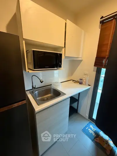 Compact kitchen with microwave and sink in modern apartment.