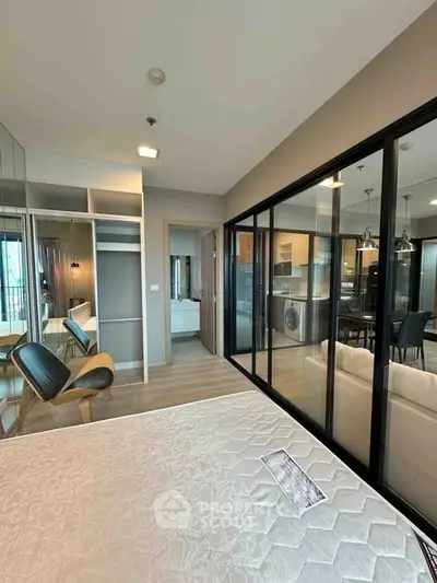 Modern bedroom with glass partition and view into stylish kitchen and living area.