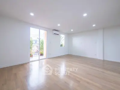 Spacious empty living room with wooden flooring and large windows for natural light.