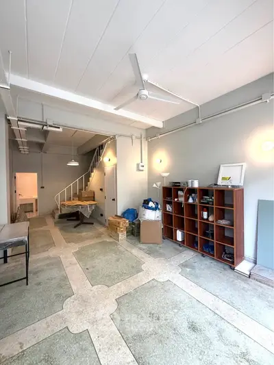 Spacious industrial-style room with high ceiling, staircase, and storage shelves, ideal for creative workspace.