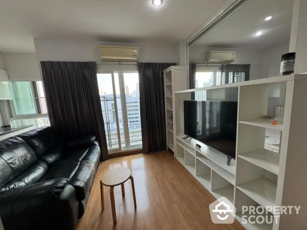 Modern living room with sleek black leather sofa and large TV, featuring city view from window.