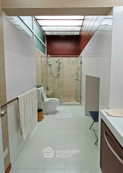 Modern bathroom with glass shower and skylight, featuring sleek design and contemporary fixtures.