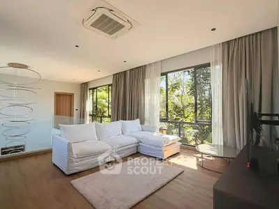 Spacious living room with large windows and modern decor, offering a serene view of lush greenery.