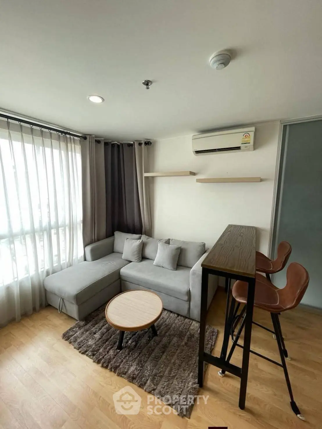 Modern living room with cozy gray sofa, stylish bar stools, and natural light from large window.
