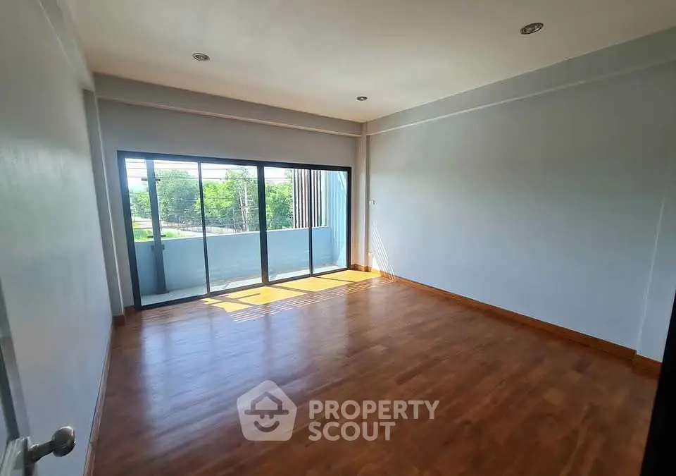 Spacious empty room with wooden flooring and large windows offering natural light and balcony access.