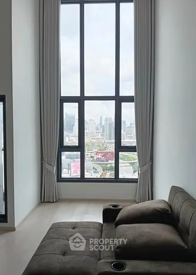 Modern living room with large window offering stunning city view, featuring sleek furniture and elegant curtains.