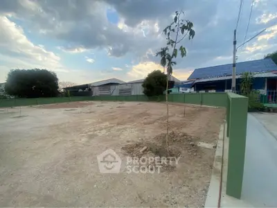 Vacant land plot with potential for development in a residential area, featuring a young tree and clear skies.