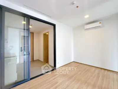 Modern empty room with wooden flooring and air conditioning, featuring a sliding glass door.