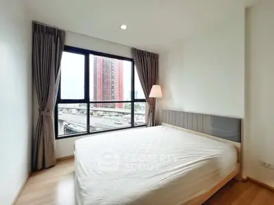 Bright bedroom with large window offering city view, featuring a cozy bed and elegant curtains.