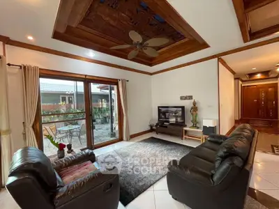 Spacious living room with leather sofas and wooden ceiling accents, opening to a cozy patio.
