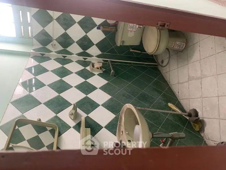 Compact bathroom with green and white tiled walls, featuring a toilet and sink.