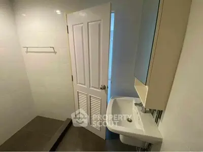 Compact bathroom with modern sink and tiled walls, featuring a sleek door and towel rack.