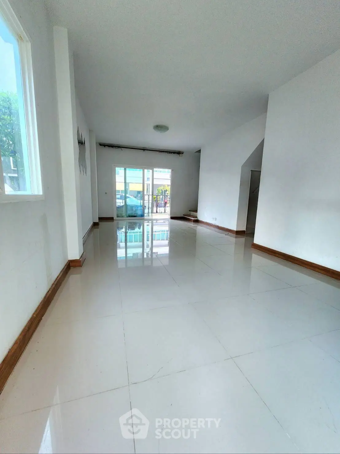 Spacious empty living room with glossy tiled floors and large windows.