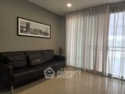 Modern living room with sleek black sofa and large window with sheer curtains.