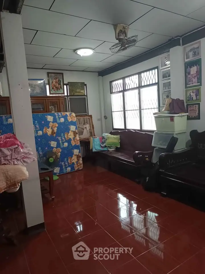 Cozy living room with tiled floor and large windows, featuring traditional wooden furniture and decorative wall art.