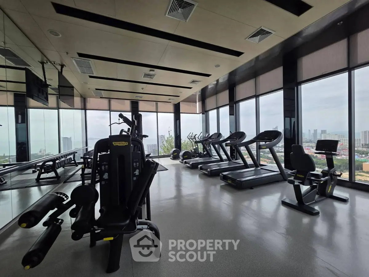 Spacious gym with modern equipment and panoramic city views, perfect for fitness enthusiasts.