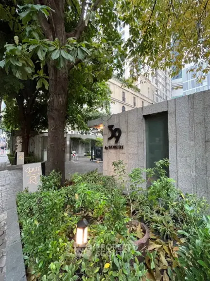 Elegant entrance of a modern building surrounded by lush greenery in an urban setting.