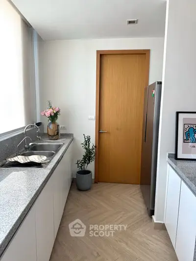 Modern kitchen with sleek countertops and stainless steel fridge, featuring a minimalist design and natural light.