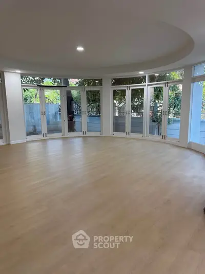 Spacious round living room with large windows and wooden flooring, offering a bright and airy ambiance.