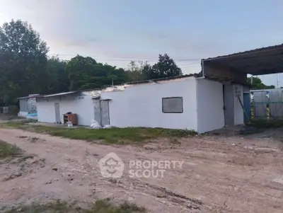 Rural property with simple white exterior and corrugated metal roof, surrounded by greenery.