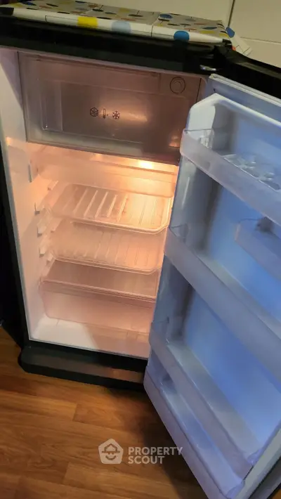 Compact refrigerator with open door showing empty shelves and interior light.