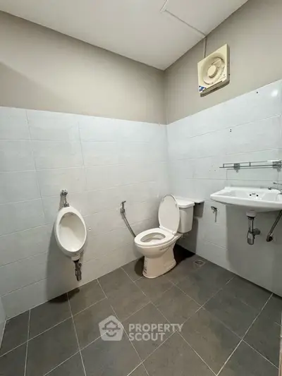 Spacious bathroom with modern fixtures and tiled flooring, featuring a toilet, urinal, and sink.