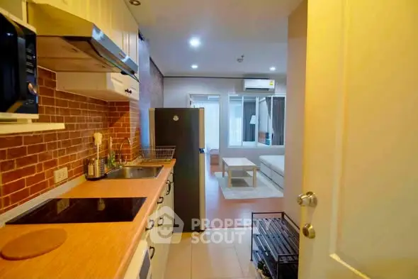 Cozy apartment kitchen with open layout leading to a modern living room, featuring sleek appliances and warm lighting.