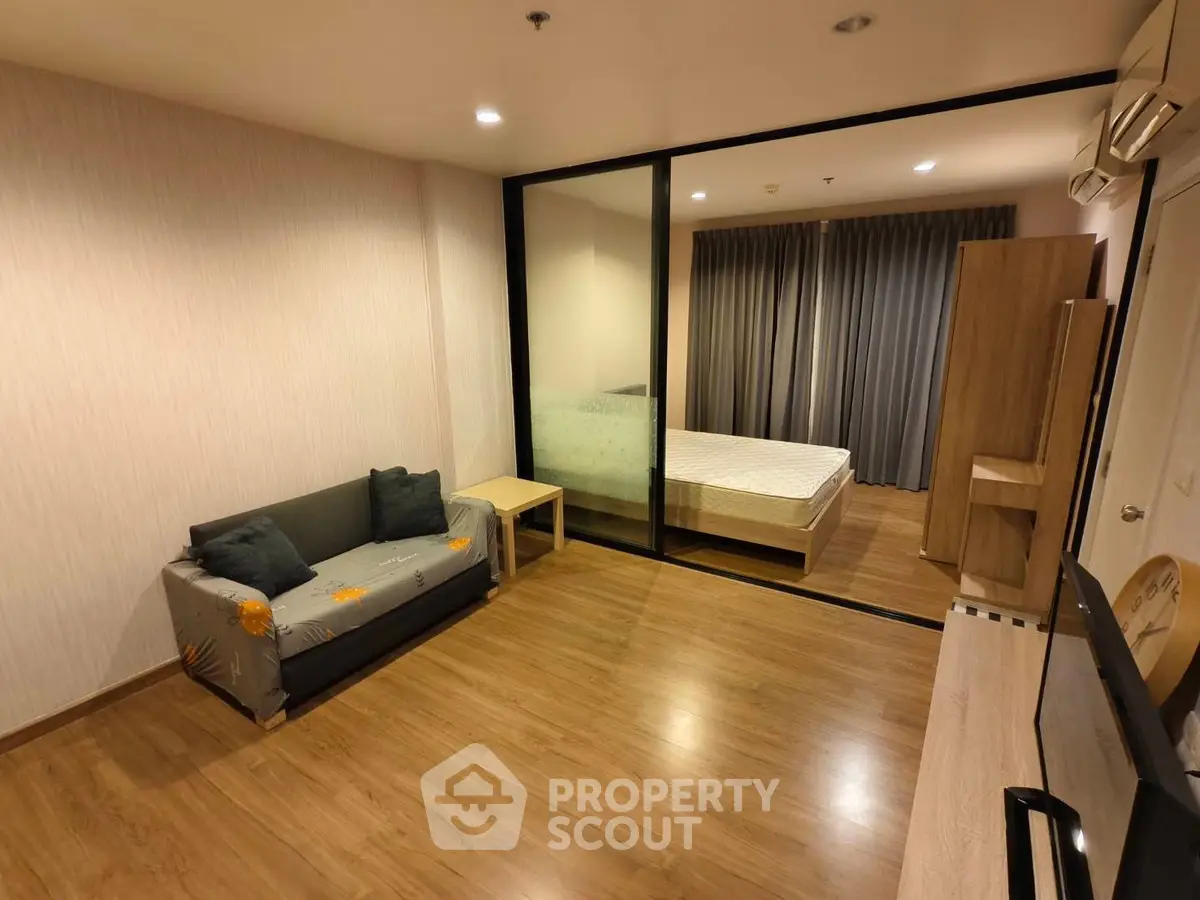 Modern studio apartment with wooden flooring and glass partition separating bedroom and living area.