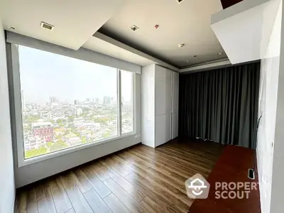 Spacious room with large window offering stunning city view and elegant wooden flooring.