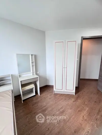 Minimalist bedroom with wooden flooring and white furniture, perfect for modern living.