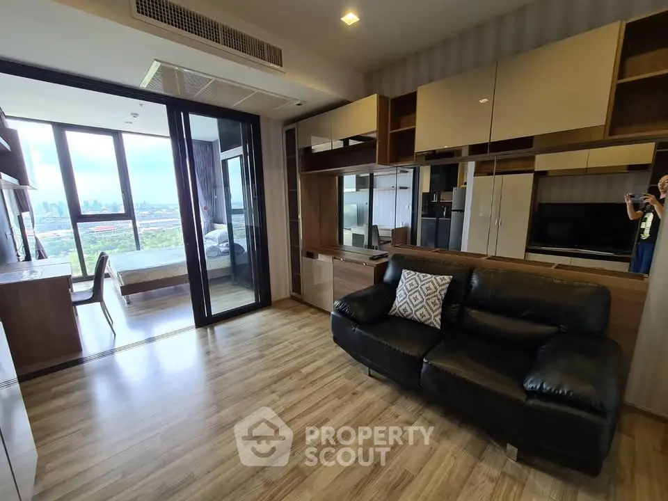 Modern living room with sleek design and city view, featuring a cozy black leather sofa and stylish cabinetry.