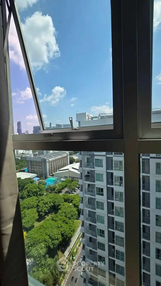 Stunning cityscape view from a high-rise apartment window with lush greenery and clear blue skies.