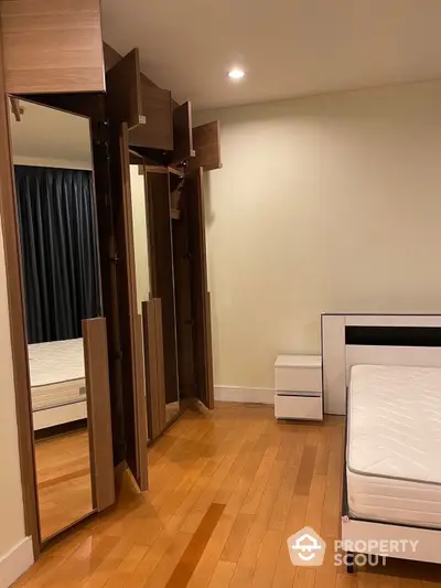 Spacious bedroom with polished hardwood floors, modern mirrored wardrobe, and a comfortable mattress set, perfect for restful nights in a serene setting.