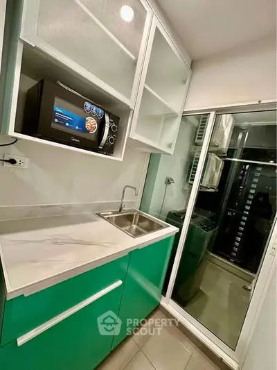 Modern compact kitchen with green cabinets and microwave, featuring a sleek design and efficient use of space.